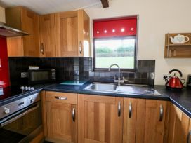 A kitchen with wooden cabinets a stainless steel oven microwave sink red kettle and window with red blind at Violet Lodge in Saltburn-by-the-Sea