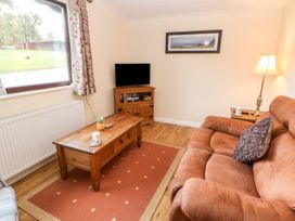 A living room with a brown sofa a wooden coffee table a television on a stand and a floor lamp at Violet Lodge in Saltburn-by-the-Sea