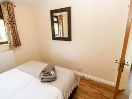 A bedroom with a bed covered in white and beige linens folded towels on the bed a mirror on the wall and a window with curtains at Violet Lodge in Saltburn-by-the-Sea