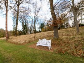 A white decorative bench on grass near trees and dry grass on a slope at Violet Lodge in Saltburn-by-the-Sea