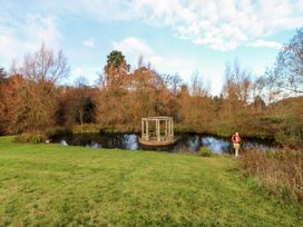 A small pond with a round stone pavilion in the center surrounded by green grass and trees at Violet Lodge in Saltburn-by-the-Sea