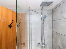 A shower with a glass door and wall tiles at Copper Beech Cottage in Torver