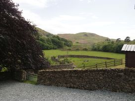 A view of a green hillside with stone walls and trees at Copper Beech Cottage in Torver