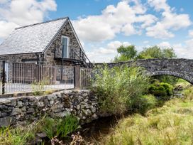 A stone building with a metal fence near a stone bridge over a stream at Glan Nug Bach in Rhydlydan near Betws-y-Coed
