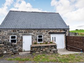 A stone building with a slate roof two white doors two windows a stone planter and a wooden fence at Glan Nug Bach in Rhydlydan near Betws-y-Coed