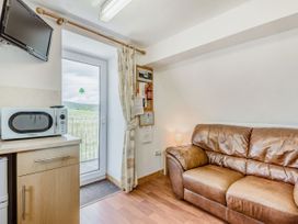 A small room with a brown leather sofa a microwave on a wooden cabinet a wall mounted television and a door with a curtain at Glan Nug Bach Rhydlydan near Betws-y-Coed