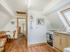 A kitchen with wooden floor, stove, countertop, sink near a window and a dining table with chairs in the background at Glan Nug Bach in Rhydlydan near Betws-y-Coed