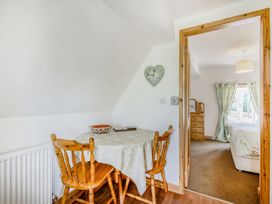A dining area with a round table and wooden chairs next to a doorway leading to a bedroom with a dresser and bed at Glan Nug Bach in Rhydlydan near Betws-y-Coed