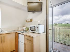 A kitchen corner with a microwave toaster bread bin and a small fridge with a glass door open to a balcony overlooking a field at Glan Nug Bach in Rhydlydan near Betws-y-Coed
