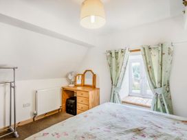 A bedroom with a bed a wooden dresser with a mirror a small fan a stool and floral curtains at Glan Nug Bach in Rhydlydan near Betws-y-Coed
