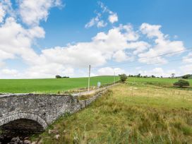 A stone bridge over a small stream with green fields and sheep near a narrow road at Glan Nug Bach in Rhydlydan near Betws-y-Coed