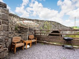 An outdoor patio with two wooden chairs a table with a parasol and a barbecue grill next to a stone wall and wooden fence by a stone bridge at Glan Nug Bach in Rhydlydan near Betws-y-Coed