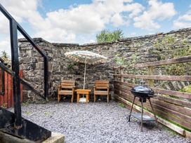 An outdoor patio with two wooden chairs a small table with an umbrella and a charcoal grill at Glan Nug Bach in Rhydlydan near Betws-y-Coed