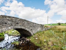 A stone arch bridge over a shallow stream with grassy fields and utility poles in the background at Glan Nug Bach in Rhydlydan near Betws-y-Coed