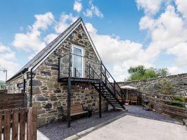 An exterior view of a stone building with an upper balcony and metal stairs a bench and patio furniture in a fenced yard at Glan Nug Bach in Rhydlydan near Betws-y-Coed