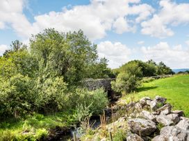 A stone bridge over a stream with trees rocks and grassy fields at Glan Nug Bach in Rhydlydan near Betws-y-Coed