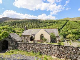 A stone church building with a graveyard and stone wall surrounded by trees and hills at St.Marys in Tal y Llyn near Dolgellau