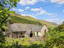 A stone church with a slate roof surrounded by gravestones and greenery with hills in the background at St.Mary's in Tal y Llyn near Dolgellau
