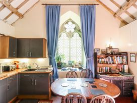 A kitchen and dining area with wooden table and chairs a bookshelf and a large arched window with blue curtains at St.Marys Tal y Llyn near Dolgellau