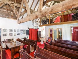 An interior view of a small chapel with wooden pews a table with brass candlesticks red curtains and exposed wooden beams at St Marys in Tal y Llyn near Dolgellau