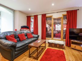 A living room with a leather sofa with red cushions a wooden coffee table a red rug and a television at St.Marys Tal y Llyn near Dolgellau