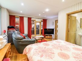 A bedroom with a bed, black leather sofa, wooden dresser, coffee table, television, red curtains and an open door to a bathroom at St.Marys in Tal y Llyn near Dolgellau
