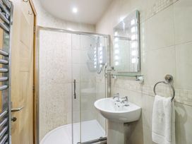 A bathroom with a shower enclosure, sink, mirror with lights, towel ring with towel and wooden door at St.Marys Tal y Llyn near Dolgellau