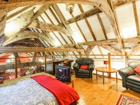 An attic bedroom with exposed wooden beams leather armchairs a wooden desk and a bed with a red blanket at St.Marys in Tal y Llyn near Dolgellau
