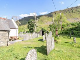 A graveyard with old headstones next to stone buildings and green hills in the background at St.Marys in Tal y Llyn near Dolgellau