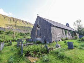 An old stone church next to a graveyard with grassy tombstones near a mountain at St.Marys in Tal y Llyn near Dolgellau
