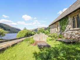 A stone church with ivy and gravestones next to a river and road at St Marys in Tal y Llyn near Dolgellau