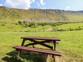 A wooden picnic table on grass with a hill and power lines in the background at St.Marys in Tal y Llyn near Dolgellau