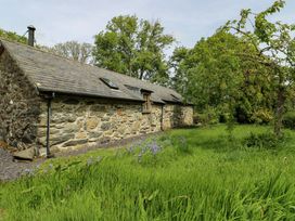 A stone cottage surrounded by grass and trees at Bythyn Ddol Hafod, Capel Curig