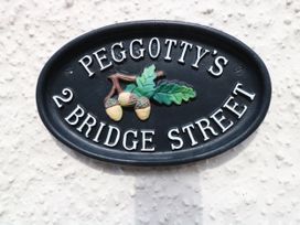 A black oval house sign with white letters reading Peggotty's 2 Bridge Street with a design of three acorns and two oak leaves at Peggotty's in Kelsale near Saxmundham