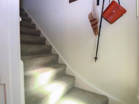 Carpeted staircase with bags and a walking stick hanging on a white wall at Peggotty's in Kelsale near Saxmundham