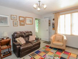 A living room with a brown leather sofa and a beige armchair near a window with curtains at Peggotty's in Kelsale near Saxmundham
