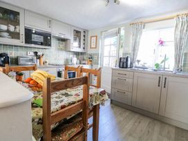 A kitchen with wooden chairs around a table and cabinets with appliances at Peggotty's Kelsale near Saxmundham