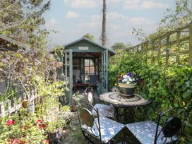 A garden area with a table and chairs in front of a wooden shed surrounded by plants and flowers at Peggotty's in Kelsale near Saxmundham