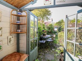 View from inside a wooden garden shed showing wicker shelves with ceramic pots and an outdoor seating area with a round table and chairs in a garden at Peggotty's in Kelsale near Saxmundham