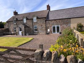 An outdoor view of a house with a lawn and flower bed at The Old Farmhouse in Lowick