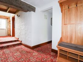 A hallway with red patterned carpet wooden bench with hooks white walls and wooden ceiling beam at Chapel Green in Polgooth