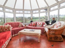 A conservatory with wicker furniture and red patterned covers overlooking green fields at Chapel Green in Polgooth