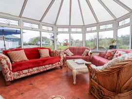 A conservatory with sofas around a wicker coffee table and windows showing a garden at Chapel Green in Polgooth