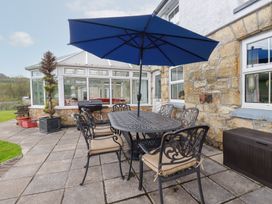 An outdoor patio with a metal table and six chairs under a blue umbrella at Chapel Green in Polgooth
