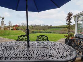 A metal outdoor table with a blue umbrella overlooking a garden with lawn and plants at Chapel Green in Polgooth