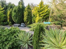 A garden with various trees and a sign at Crow's Nest Cottage in Tynygongl near Benllech
