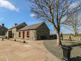 An outdoor area with a stone house and tree at Poppy Cottage in Caeathro near Caernarfon