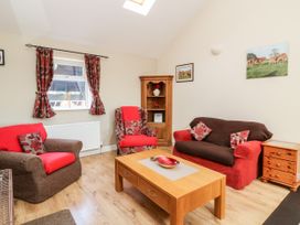 A living room with a wooden coffee table sofa armchairs and cupboard with curtains on window at 2 Pines Farm Cottages Ulleskelf