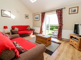 A living room with two sofas covered in red throws a wooden chest coffee table a television on a wooden stand and a door opening to a garden at 2 Pines Farm Cottages Ulleskelf