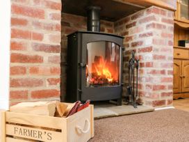 A wood burning stove with fire inside a brick fireplace with fire tools and a wooden box of firewood at 2 Pines Farm Cottages in Ulleskelf
